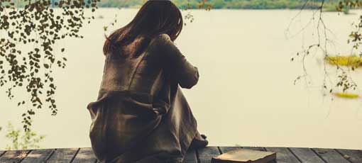 Frau sitzt einsam am See