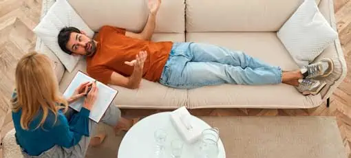 Psychologischer Heilpraktiker | Junge depressive Mann an der Rezeption einer weiblichen Psychologin während einer psychischen Sitzung auf dem Sofa liegen. 